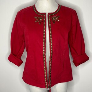 Puede incluir: Una chaqueta roja con cremallera con ribete de cadena dorada y adornos dorados alrededor del cuello.