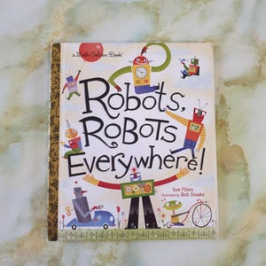 May include: A children's book titled "Robots, Robots Everywhere!" by Sue Fliess, illustrated by Bob Staake. The cover features a whimsical design with various robot illustrations and the title in large, bold letters. The book has a gold spine.