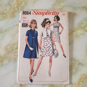 May include: Vintage Simplicity sewing pattern, featuring three women in stylish dresses. The pattern is labelled "8064" and includes sizing information for Misses, size 10, and a bust size of 82.5 cm. The cover has a retro design.