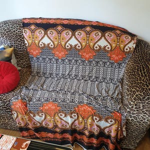 May include: A black, white and orange patterned fabric with paisley designs. The fabric is draped over a leopard print sofa.