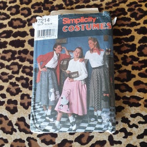 May include: A vintage Simplicity Costumes sewing pattern packet featuring a retro design. The packet showcases a picture of three women in poodle skirts and sweaters. The packet is on a leopard print background.