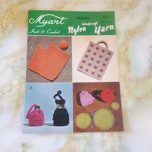 May include: A vintage knitting and crocheting pattern book featuring Myart Nylon Yarn. The cover shows a variety of crocheted items, including a bag, a hat, a bottle cover, a dress, and placemats. The book is titled "Myart Nylon Yarn" and is labelled "handcraft book 14".