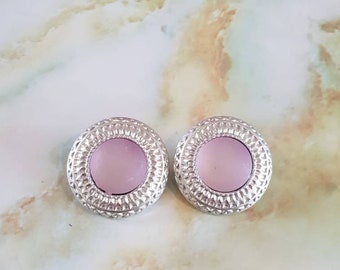 Earings 1980's clip on. Ornate textured silvertone in a circle shape, surrounding a pale pink lucite centre.