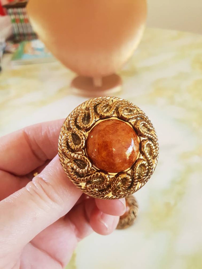 Earings 1980/'s clip on Ornate textured goldtone surrounding a caramel colored acrylic centre.