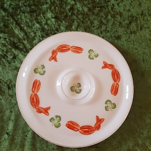 Könnte beinhalten: Weiße Keramik-Servierplatte mit einer kleineren, runden Schale in der Mitte. Die Platte hat einen goldenen Rand und ist mit roten und grünen Malereien verziert.