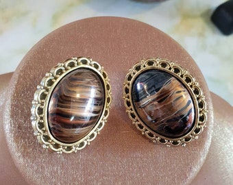 Earings 1980's clip on. Ornate goldtone acrylic in an oval shape, framing a gold/brown faux stone centre.