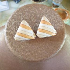 May include: A pair of triangular shaped earrings with a white and orange striped pattern.