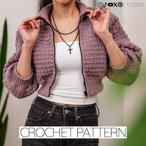 May include: A cropped, mauve-colored crochet jacket with a black zipper and ribbed cuffs. The jacket has a textured stitch pattern and is worn over a white top and black jeans. The words "CROCHET PATTERN" are displayed at the bottom of the image.