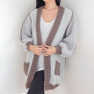 TCDDIY crochet pattern for an Oversized Reversible Cardigan featuring a ribbed two-toned design, pockets, crafted using Lion Brand Pound of Love yarn in Elephant Grey and Taupe.