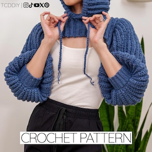 Puede incluir: Un bolero con capucha de ganchillo azul con mangas largas. El bolero presenta una textura acanalada y detalles de cordón. El texto "CROCHET PATTERN" se muestra en la parte inferior de la imagen.