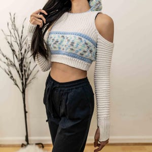 TCDDIY crochet pattern for a cold shoulder cropped hoodie with herringbone hood and thumbholes, crafted using Baby Bernat Sport yarn in White, Cool Blue, and Baby Blue.