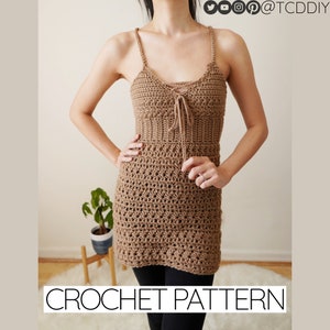 May include: A crochet dress pattern featuring a brown crocheted dress with a lace-up detail at the neckline. The dress is sleeveless and has a fitted bodice and a flowing skirt. The pattern is available for download.