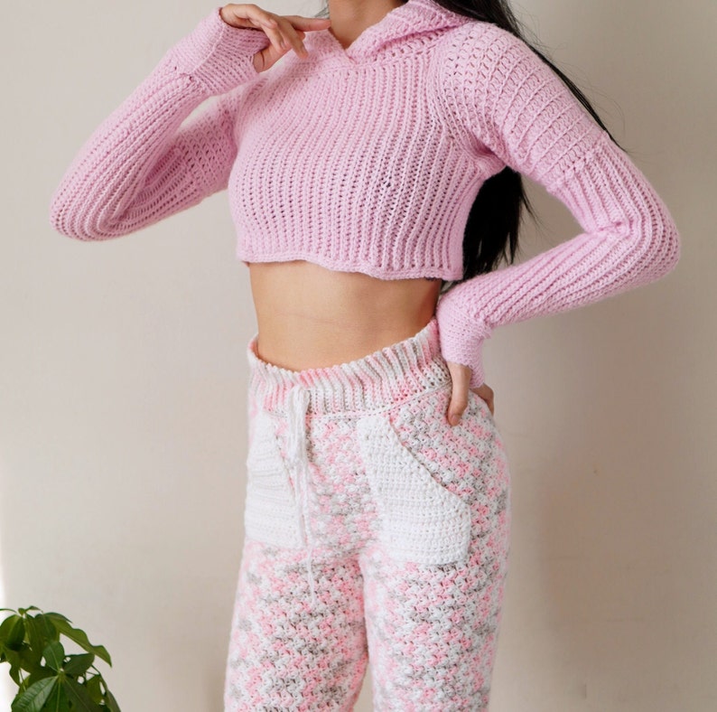 TCDDIY crochet pattern for a Long Sleeve Cropped Hoodie with thumbhole cuffs, ribbed sleeves, and customizable sizing, crafted using Lion Brand Pound of Love yarn in Pastel Pink.