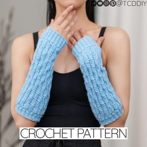 May include: A pair of light blue crochet arm warmers. The arm warmers have a cable knit pattern. CROCHET PATTERN is written in white text at the bottom of the image.