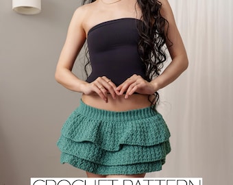 May include: A teal crochet mini skirt with layered ruffles. The skirt is paired with a black tube top. The text "CROCHET PATTERN" is displayed in a white font at the bottom of the image. The image also contains social media icons.
