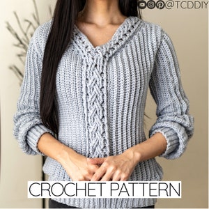 May include: A gray crochet sweater with a cable knit pattern and a v-neck. The sweater has long sleeves and a ribbed texture.