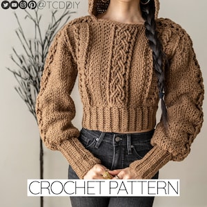 May include: A brown crocheted sweater with a hood and long sleeves. The sweater has a cable knit pattern and a cropped length. The sweater is worn over a pair of black jeans. CROCHET PATTERN is written in white text at the bottom of the image.