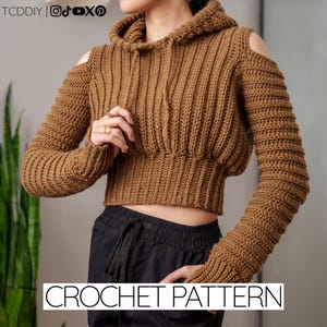 Puede incluir: Una sudadera con capucha de ganchillo marrón con hombros descubiertos. El suéter corto presenta mangas largas y una capucha con cordón. El texto "CROCHET PATTERN" se muestra en la parte inferior de la imagen.