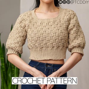 Könnte beinhalten: Ein beigefarbener, gecroppter Häkelpullover mit quadratischem Ausschnitt und kurzen, gepufften Ärmeln. Der Pullover hat ein strukturiertes Korbgeflechtmuster. Die Worte "CROCHET PATTERN" werden in weißen Blockbuchstaben am unteren Bildrand angezeigt.
