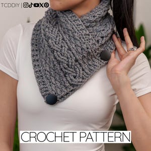 Puede incluir: Un cuello de ganchillo gris con un patrón texturizado y dos botones grandes de color gris oscuro. El cuello se lleva alrededor del cuello y forma parte de un patrón de ganchillo. El texto "CROCHET PATTERN" se muestra en la parte inferior de la imagen.