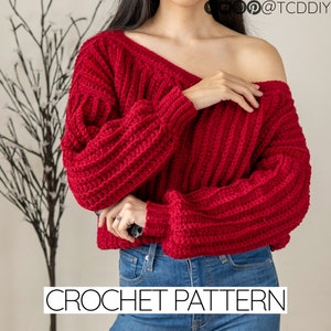 Peut inclure: Un pull en crochet rouge à col large et manches longues. Le pull est court et ample. CROCHET PATTERN est écrit en blanc en bas de l'image.