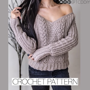 Puede incluir: Un suéter de ganchillo con un patrón de punto de cable y un cuello en V profundo. El suéter es de color marrón claro y tiene mangas largas. El suéter se muestra en una modelo que lleva pantalones vaqueros negros.