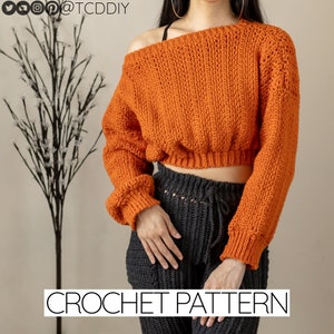 Puede incluir: Un patrón de crochet para un suéter corto de hombros descubiertos en color naranja quemado. El suéter tiene mangas largas con un puño ligeramente fruncido. El patrón está disponible en el sitio web @TCDDDIY.