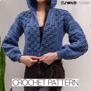 May include: A blue crochet hooded cardigan with a textured weave design. The cropped jacket has long sleeves and a deep V-neck. The text "CROCHET PATTERN" is displayed at the bottom of the image.
