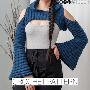 Puede incluir: Un top de crochet azul con capucha y mangas acampanadas. El top tiene un corte en el pecho y es corto a la cintura.