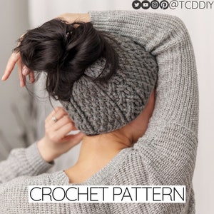 Puede incluir: Un gorro gris de ganchillo con espacio para un moño, diseñado para ser usado con un moño desordenado. El gorro está hecho con un hilo grueso y tiene un patrón de punto de cable. La imagen incluye el texto "CROCHET PATTERN".