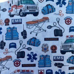 K&ouml;nnte beinhalten: Ein wei&szlig;er und blauer Stoff mit einem sich wiederholenden Muster aus medizinischen Symbolen, darunter ein rotes Kreuz, ein Stern des Lebens und die W&ouml;rter "Paramedic", "EMS" und "EMT". Der Stoff zeigt auch Bilder von Krankenwagen, medizinischen Taschen und anderen medizinischen Ger&auml;ten.