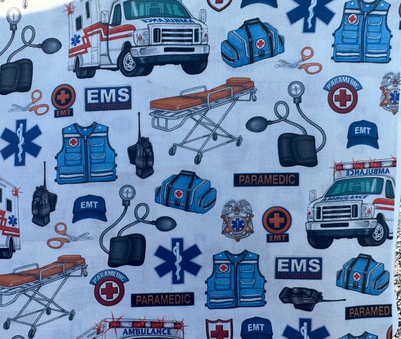 K&ouml;nnte beinhalten: Ein wei&szlig;er und blauer Stoff mit einem sich wiederholenden Muster aus medizinischen Symbolen, darunter ein rotes Kreuz, ein Stern des Lebens und die W&ouml;rter "Paramedic", "EMS" und "EMT". Der Stoff zeigt auch Bilder von Krankenwagen, medizinischen Taschen und anderen medizinischen Ger&auml;ten.