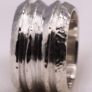 Op de afbeelding: Een zilveren ring met een getextureerde, gehamerde afwerking. De ring heeft een reeks verticale ribbels die rond de band lopen. Het metaal heeft een heldere, reflecterende kwaliteit. Een eenvoudig maar opvallend sieraad voor dagelijks gebruik.
