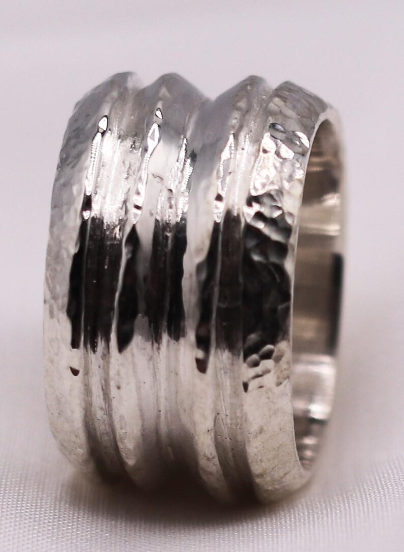 Op de afbeelding: Een zilveren ring met een getextureerde, gehamerde afwerking. De ring heeft een reeks verticale ribbels die rond de band lopen. Het metaal heeft een heldere, reflecterende kwaliteit. Een eenvoudig maar opvallend sieraad voor dagelijks gebruik.