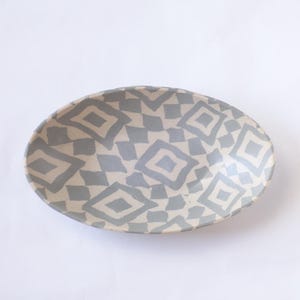 May include: Oval ceramic serving dish with a light beige background and a repeating pattern of gray diamond shapes. The dish has a slightly raised edge and a smooth surface.