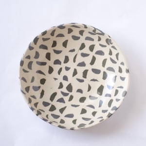 Op de afbeelding: Een witte keramische mok met een zwarte handgreep en de tekst "But First, Coffee" in een vetgedrukte, zwarte letter. De mok staat op een houten oppervlak. De mok lijkt ongeveer 355 ml te bevatten.