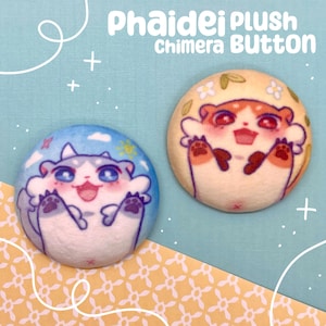 以下が含まれることがあります： 漫画のキメラデザインの丸いぬいぐるみボタンが2つ。1つのボタンは青い背景に白と灰色のキメラ、もう1つは黄色い背景にオレンジと白のキメラがあります。「Phaidei Plush Chimera Button」という文字が上部にあります。