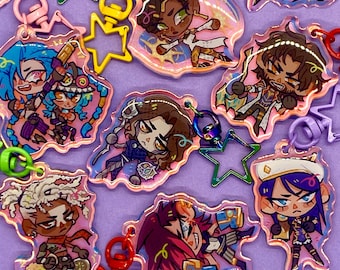 May include: A set of colorful character charms with a holographic finish. The charms feature various characters with different expressions and poses. The charms are attached to keychains with star-shaped metal rings.