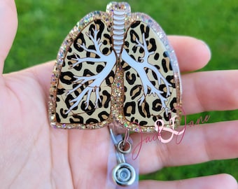 May include: A leopard print glitter resin badge holder shaped like a pair of lungs. The holder has a clear plastic strap and a silver metal clip.