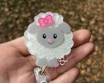 May include: A white glitter lamb with a pink bow, a cute cartoon face, and a clear plastic retractable badge holder.