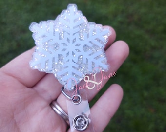 May include: A snowflake-shaped badge reel with a clear plastic strap and a metal clip. The snowflake is white with glitter accents. The text "Jack & Jane" is visible on the badge reel.