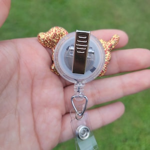 May include: A gold and red glitter dog charm attached to a clear retractable badge holder with a silver clip.