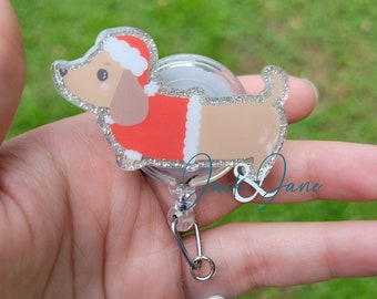 May include: A clear plastic retractable badge holder with a silver clip and a glitter-covered dachshund wearing a red and white Santa suit.
