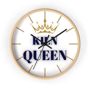 May include: A white round clock with a wooden frame. The clock face has a gold crown and the text "KİLN QUEEN" in navy blue.