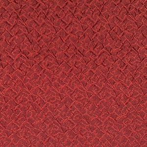 May include: Close-up of a textured, brick-red fabric. The pattern is a repeating, woven design of small, raised squares. The fabric has a slightly shiny appearance, and the color is a deep, warm red.