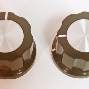 May include: Two black plastic knobs with a silver center and a white line on the side. The knobs have a scalloped edge.
