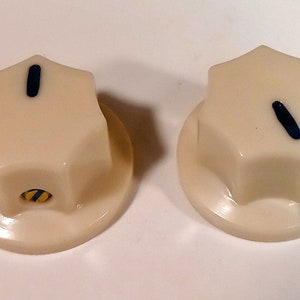 May include: Two white plastic knobs with a six-pointed star shape. Each knob has a black line on the top and a yellow and black stripe on the bottom.