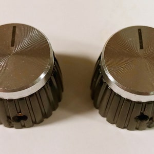 May include: Two black and silver knobs with a ribbed base and a silver top. The knobs have a single line etched on the top.