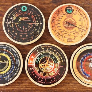 May include: A collection of five vintage-style wooden coasters, each with a radio dial design. The coasters feature different colour schemes and brand names, such as Zenith and Crosley. They are round with a light wood border.