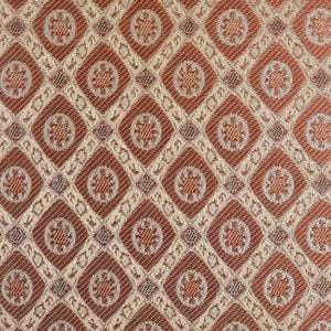 May include: Close-up of a woven fabric with a repeating diamond pattern. The diamonds are a reddish-brown colour and are outlined with a beige colour. Each diamond contains a floral design in the centre.